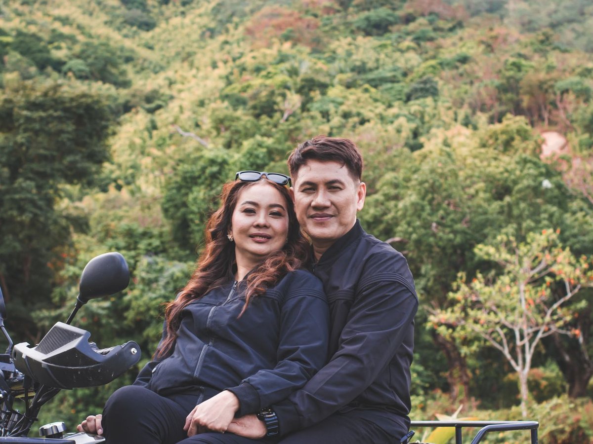 Smiling couple on an ATV after a Bali jungle ride with tropical hillside behind them