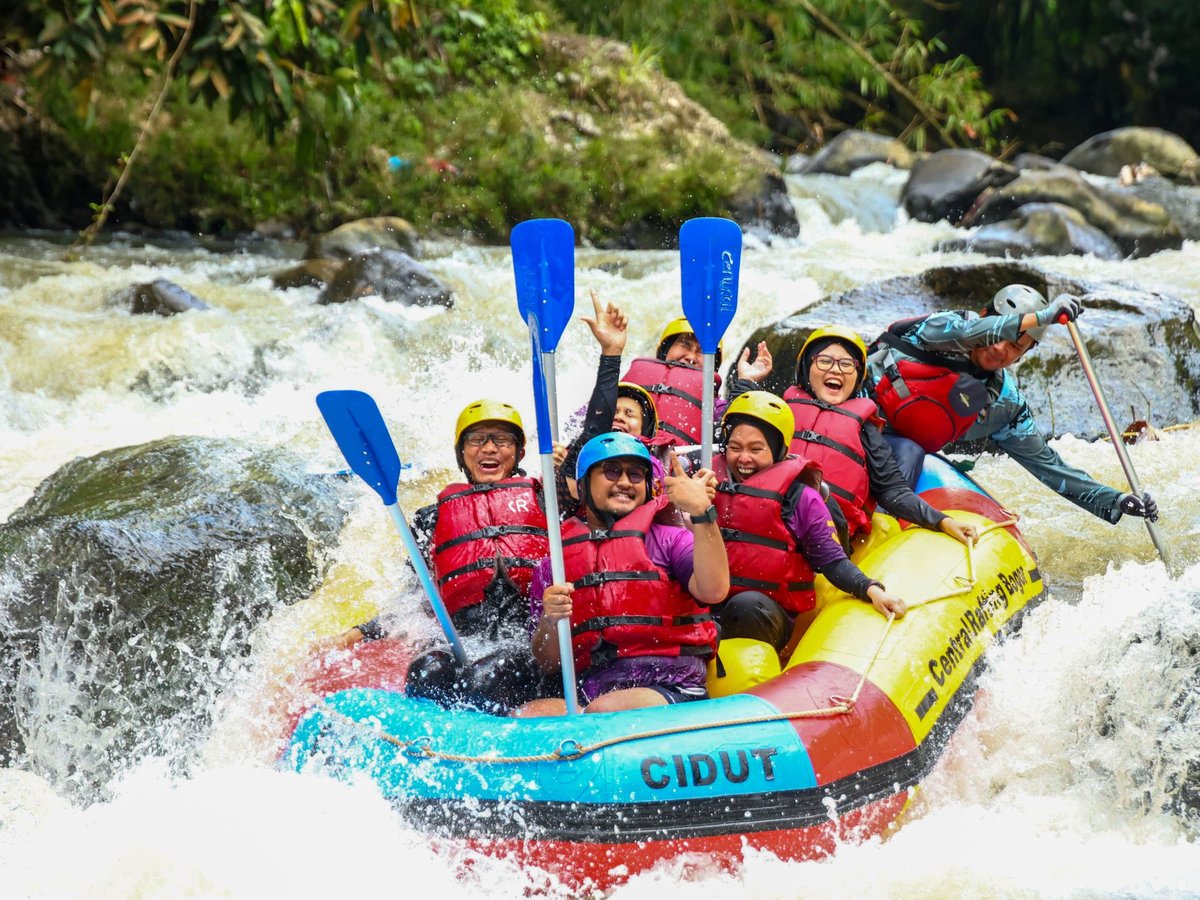 Group in life jackets paddling a colourful raft through white-water rapids in a jungle gorge