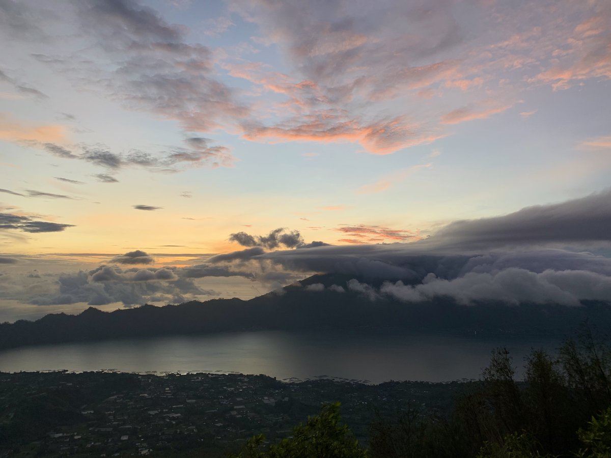 Sunrise from the summit of Mount Batur in Bali with clouds filling the caldera and Mount Agung behind